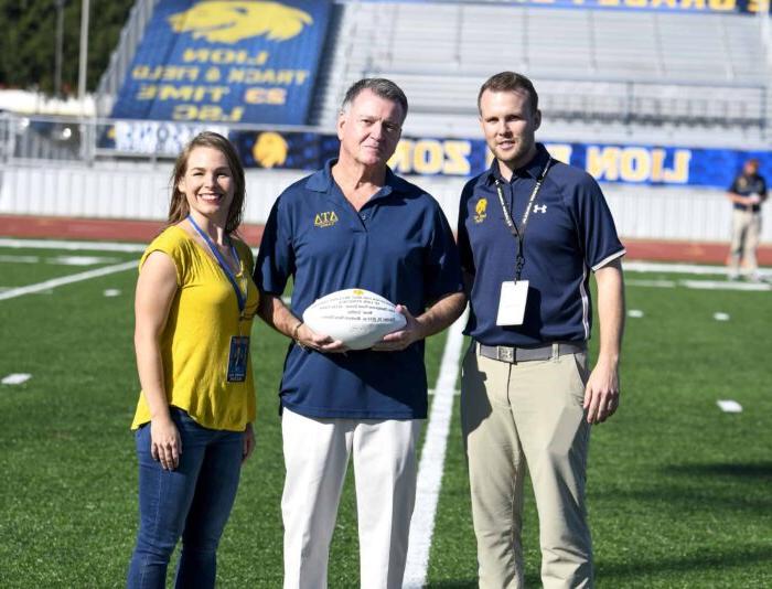 A male donor is presented with a football. He is between two other staff members from A&M-Commerce.